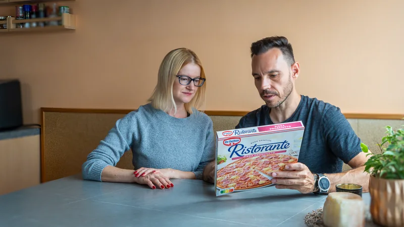 Sascha und eine Klientin sitzen am Küchentisch und schauen gemeinsam auf die Verpackung einer Tiefkühlpizza